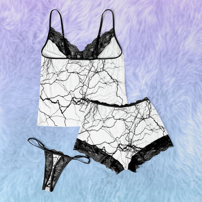 Wonder Skull White Lightning 3-Piece Gothic Sleepwear Set blends edgy design with elegant details. This set includes a white cami adorned with a bold lightning print, Gothic-inspired pajama shorts with stylish lettering, and delicate black lace accents. A coordinating thong completes the look, making it an ideal choice for those who appreciate loungewear that’s equal parts artistic, fashionable, and comfortable.